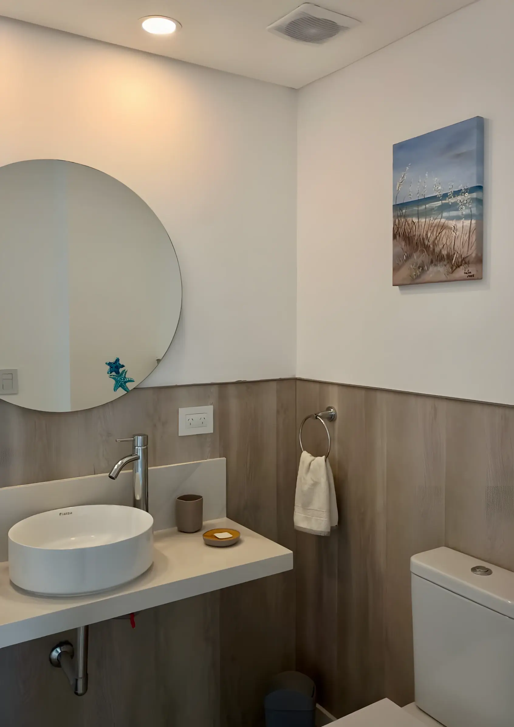 Baño con espejo redondo, bacha de apoyo y cuadro